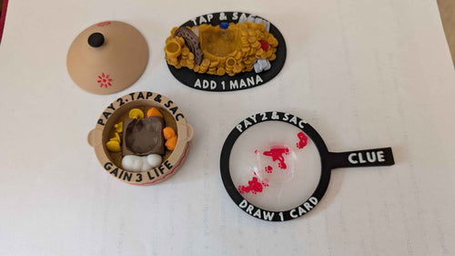 3 MTG Artifact Tokens: with instructions. Clue Token in the shape of a magnifying glass with a D6 slot in the middle. Treasure token in the shape of a treasure pile with other valuables with a d20 slot in the middle. Food token in the shape of a cooking stew with a removable D20 slot.